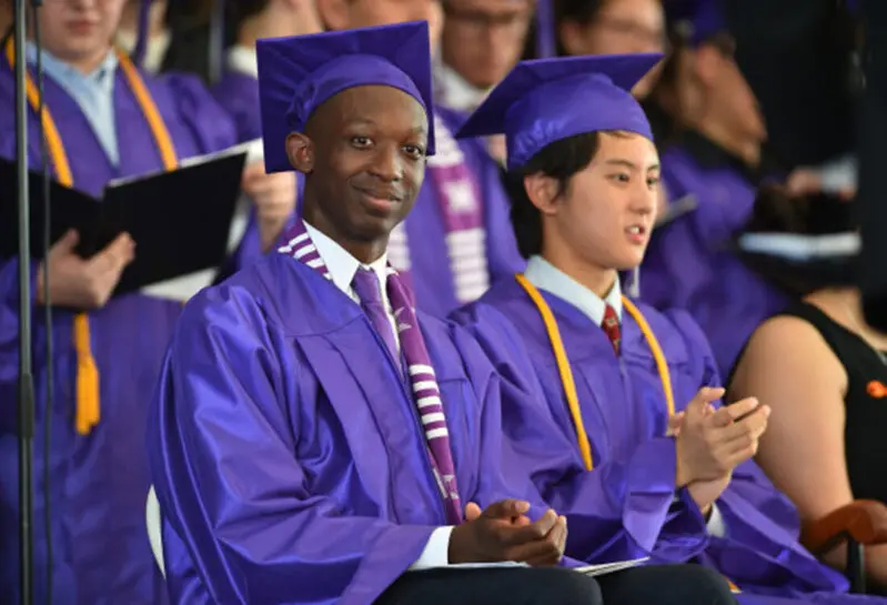 Graduates donning purple academic regalia clap.